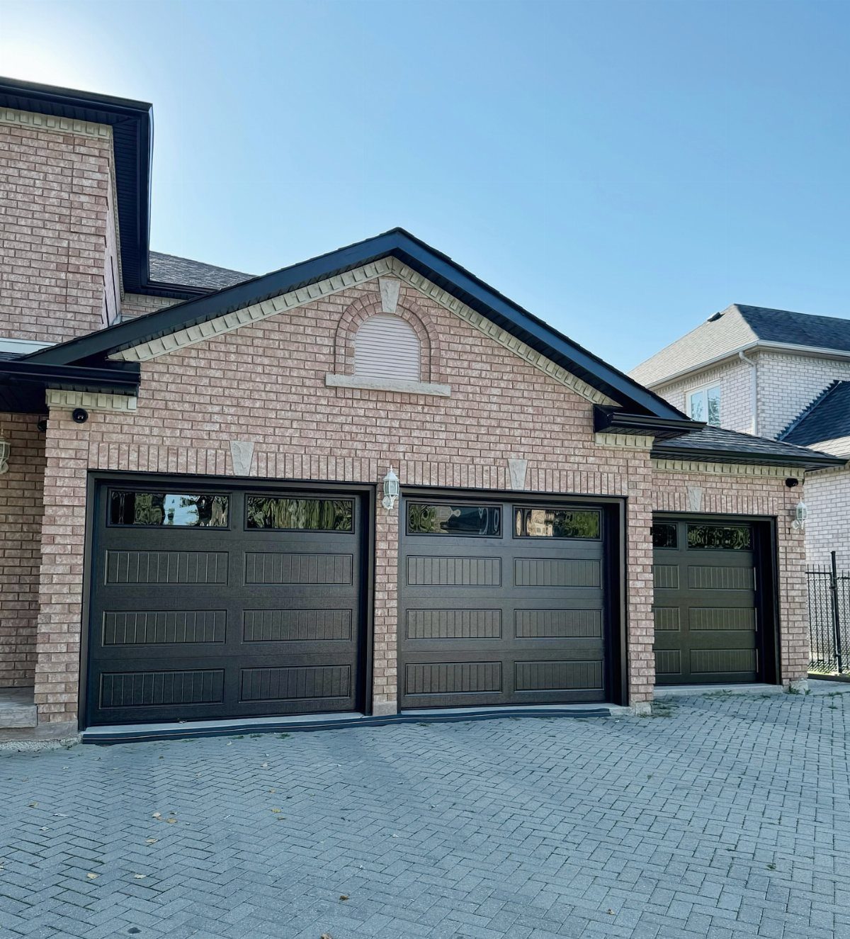 3 Car Garage Design: 8 Ideas for Style and Function 7 A three-car garage with dark brown doors on a light brick house with a cobblestone driveway.