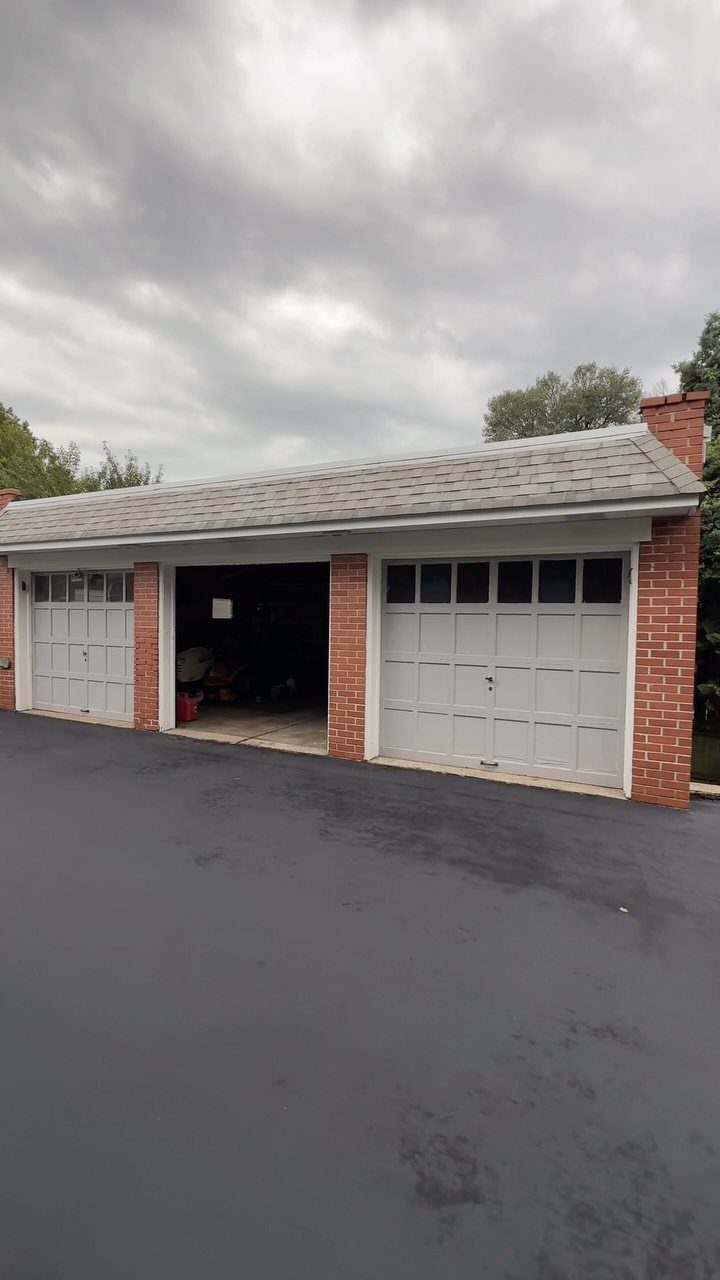 3 Car Garage Design: 8 Ideas for Style and Function 1 A red brick detached garage with two white doors and an asphalt driveway under cloudy skies.