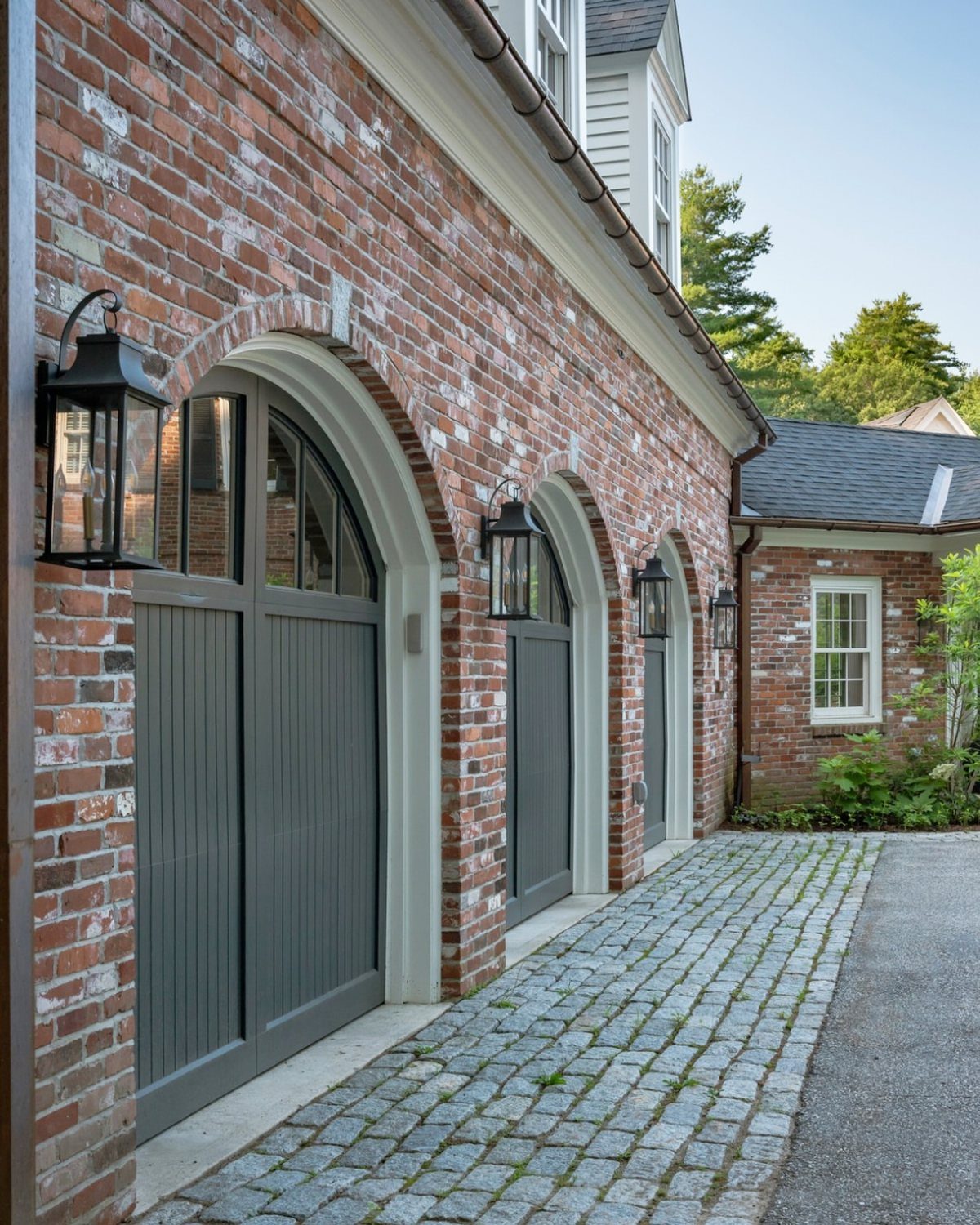 3 Car Garage Design: 8 Ideas for Style and Function 2 A brick garage with three arched grey doors and black lantern lights on a cobblestone driveway.