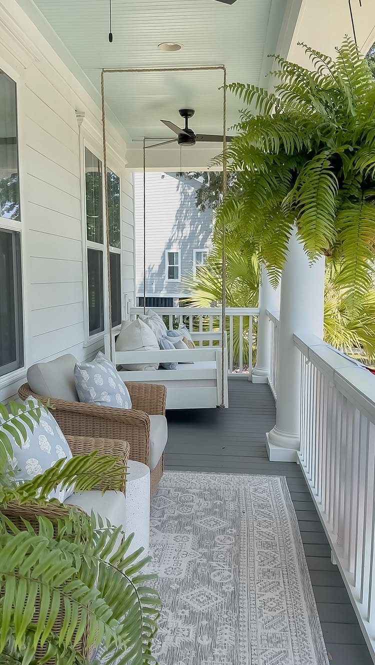 A cozy white porch with a hanging swing, wicker chairs, and green ferns.