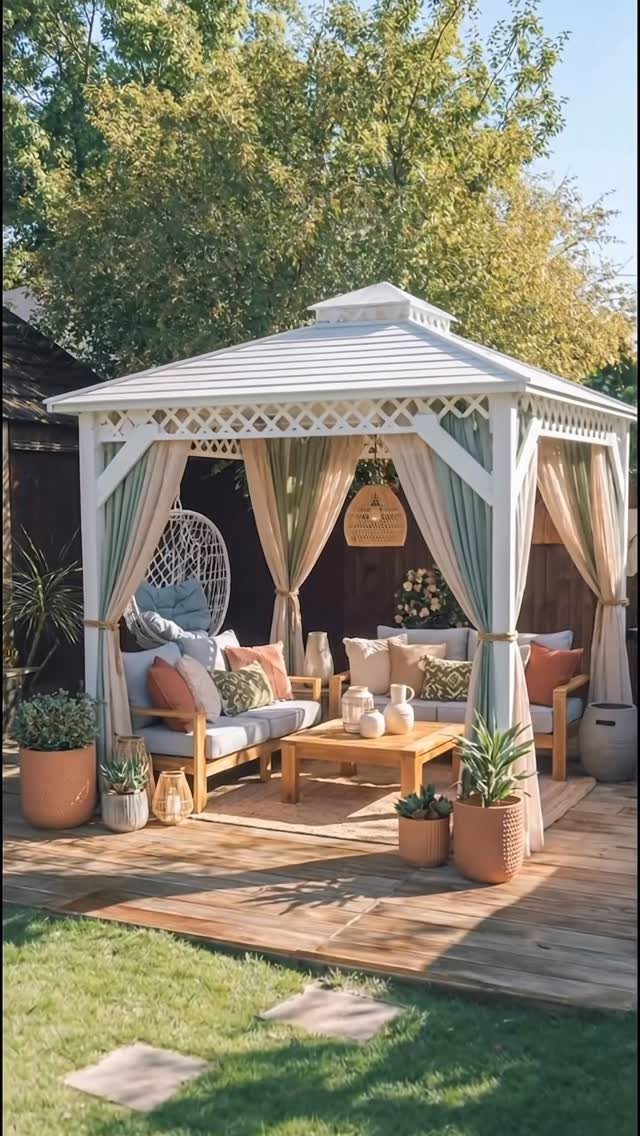 White wooden gazebo with green curtains and comfortable outdoor furniture on a wooden deck.