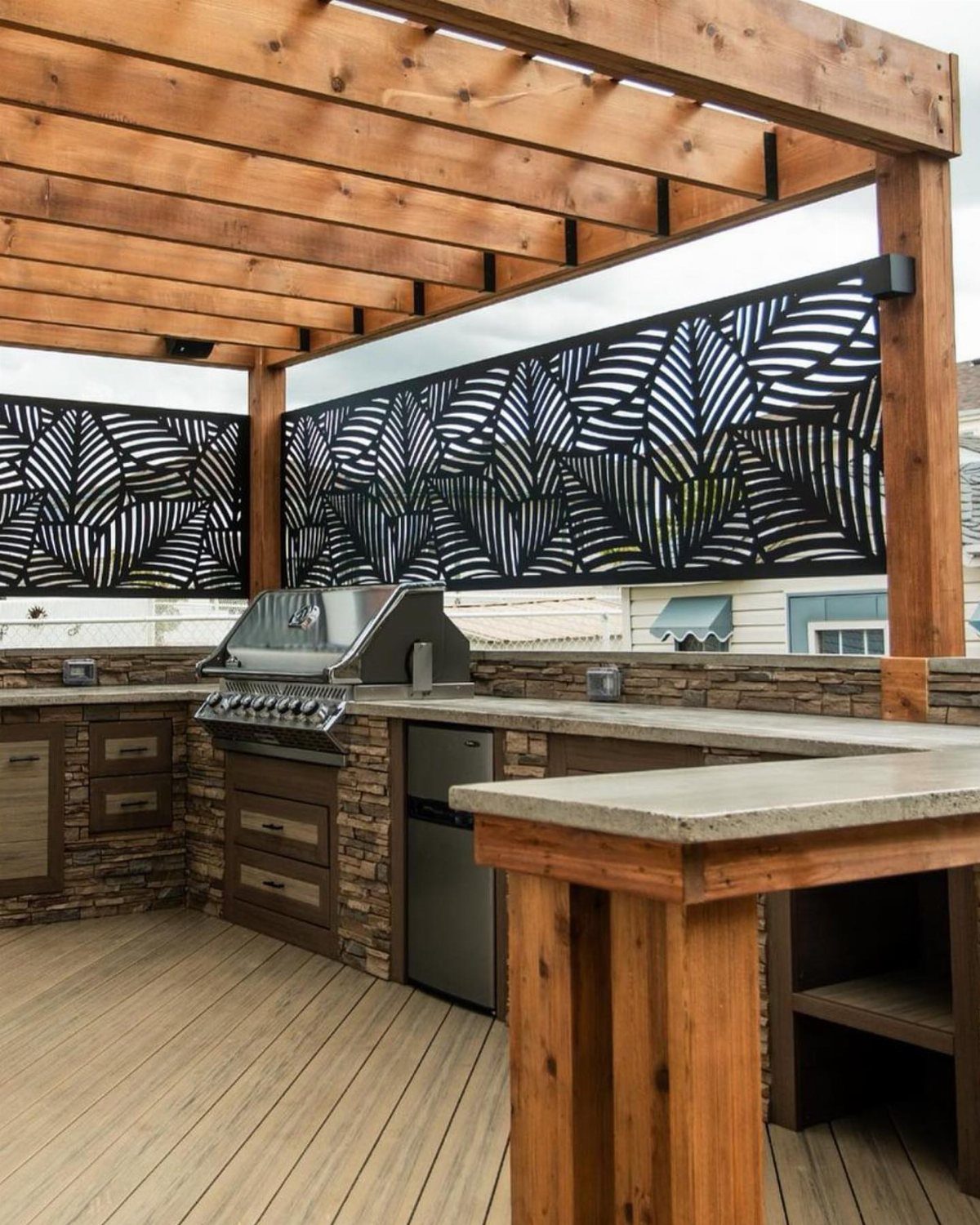 Black leaf-patterned privacy screens installed on a wooden deck pergola overlooking an outdoor kitchen.