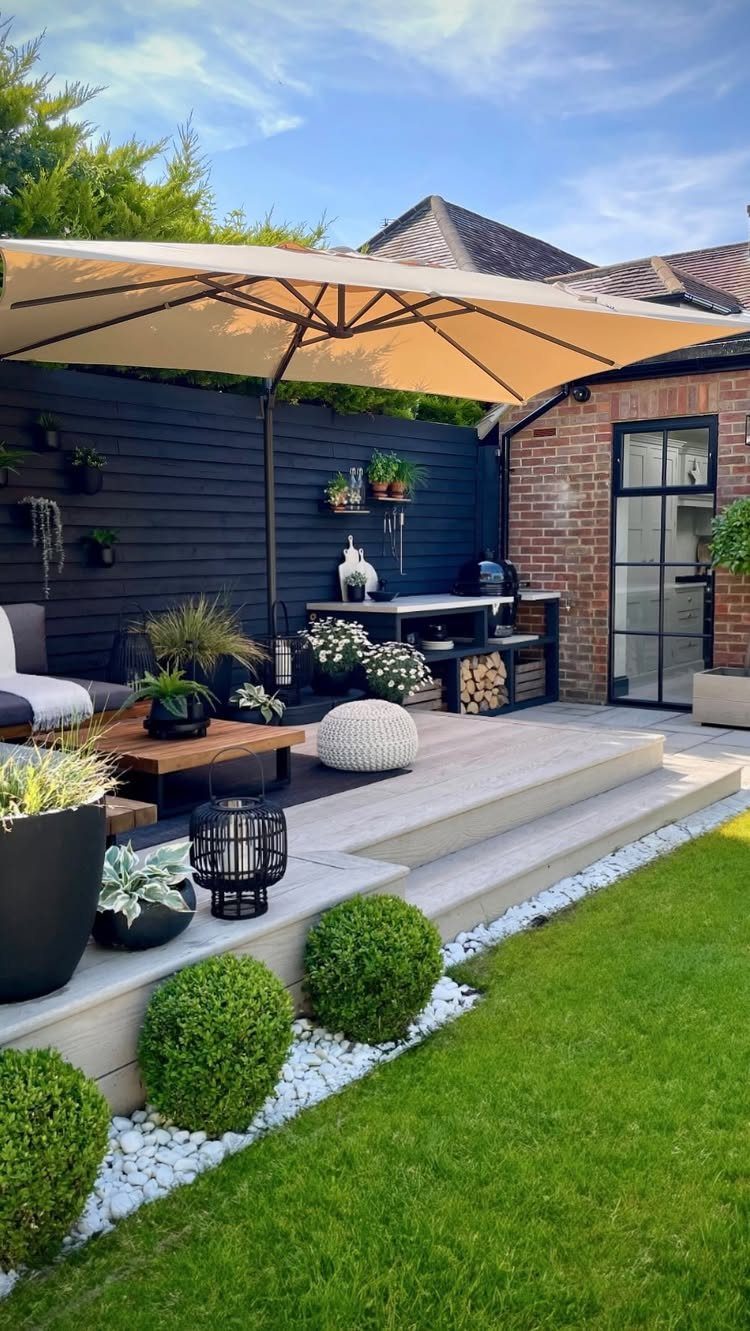 A modern multi-level wooden deck with a large tan umbrella and various potted plants.