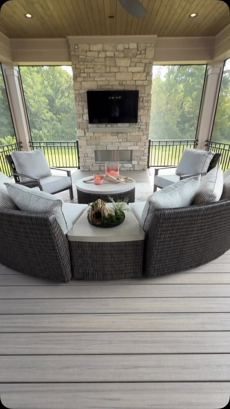 Wicker outdoor sectional and armchairs arranged around a stone fireplace on a covered deck.