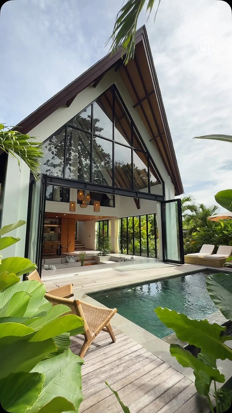 Wooden deck and swimming pool beside a modern house with large glass windows and tropical plants.