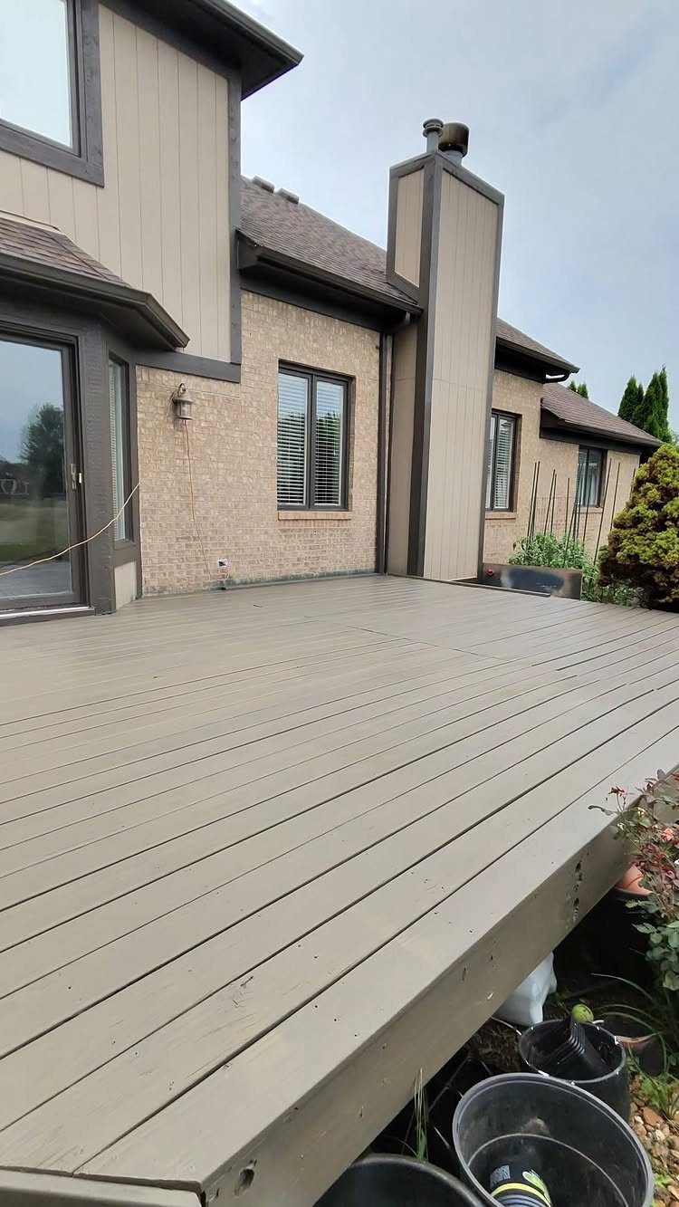 A large wooden deck with a smooth taupe stain attached to a tan house.