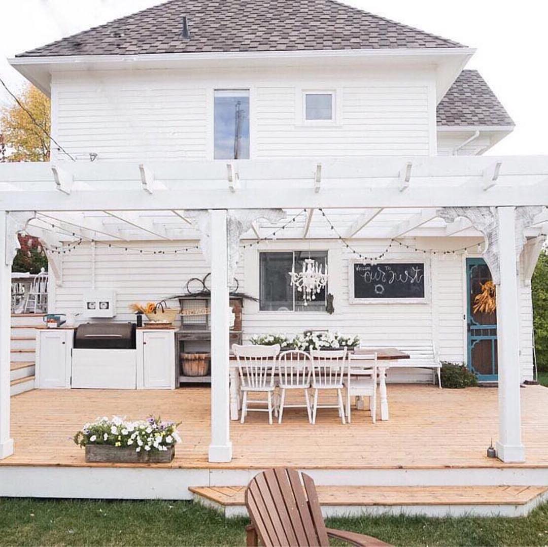 White wooden deck with dining furniture, string lights, and decorative plants under a pergola.