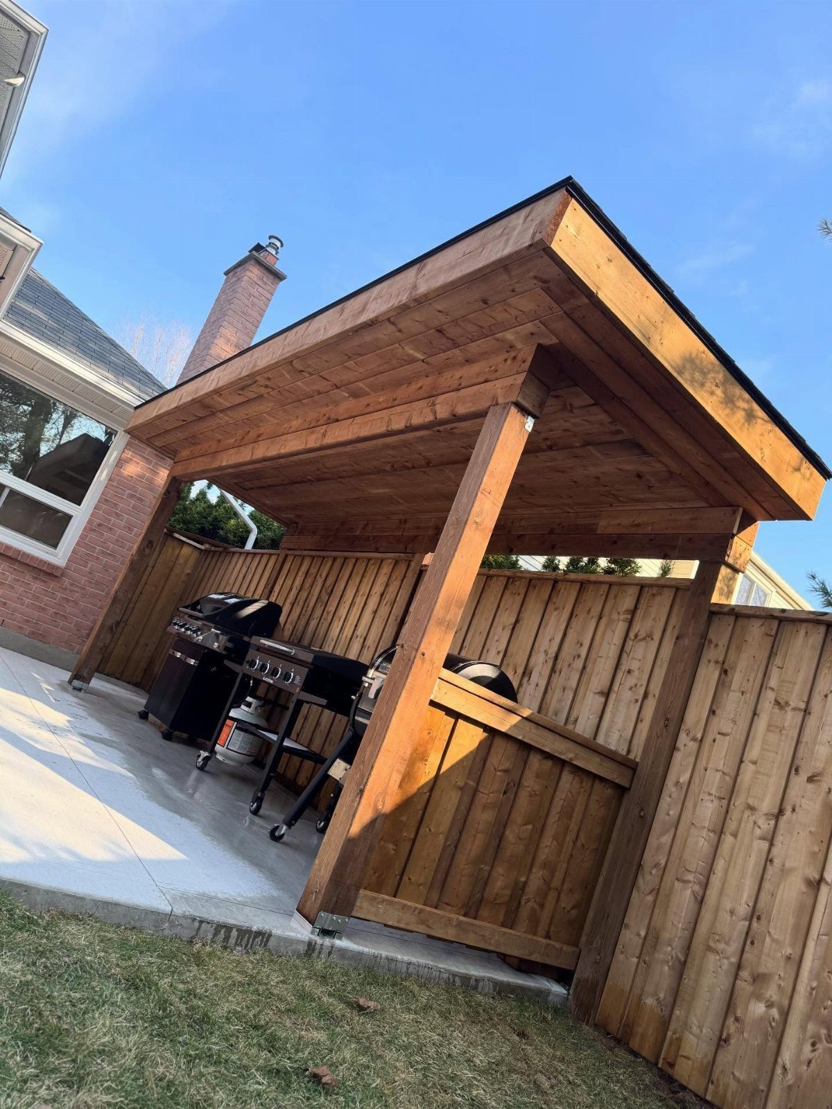 12 Backyard BBQ Ideas for Grill Area and Patio Layout 4 A wooden covered cooking station protecting a black gas grill on a concrete patio.