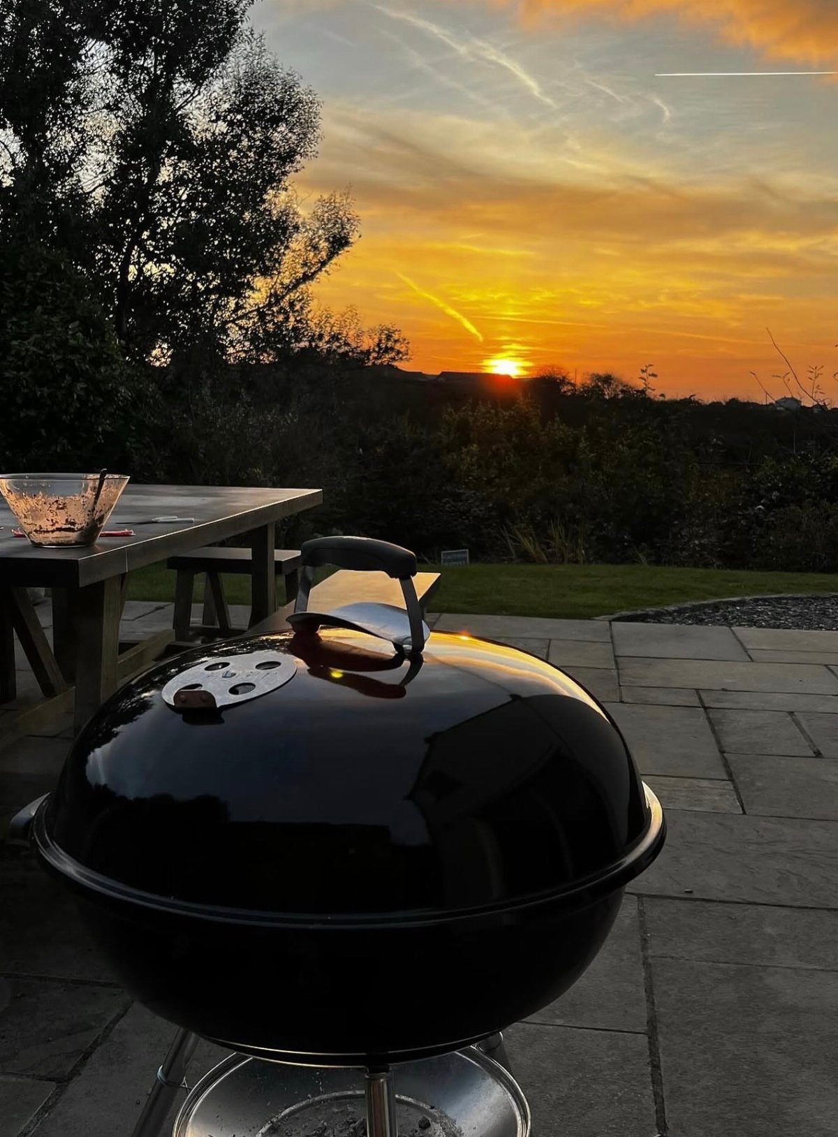 12 Backyard BBQ Ideas for Grill Area and Patio Layout 11 Black kettle grill on a stone patio overlooking a scenic sunset over trees.