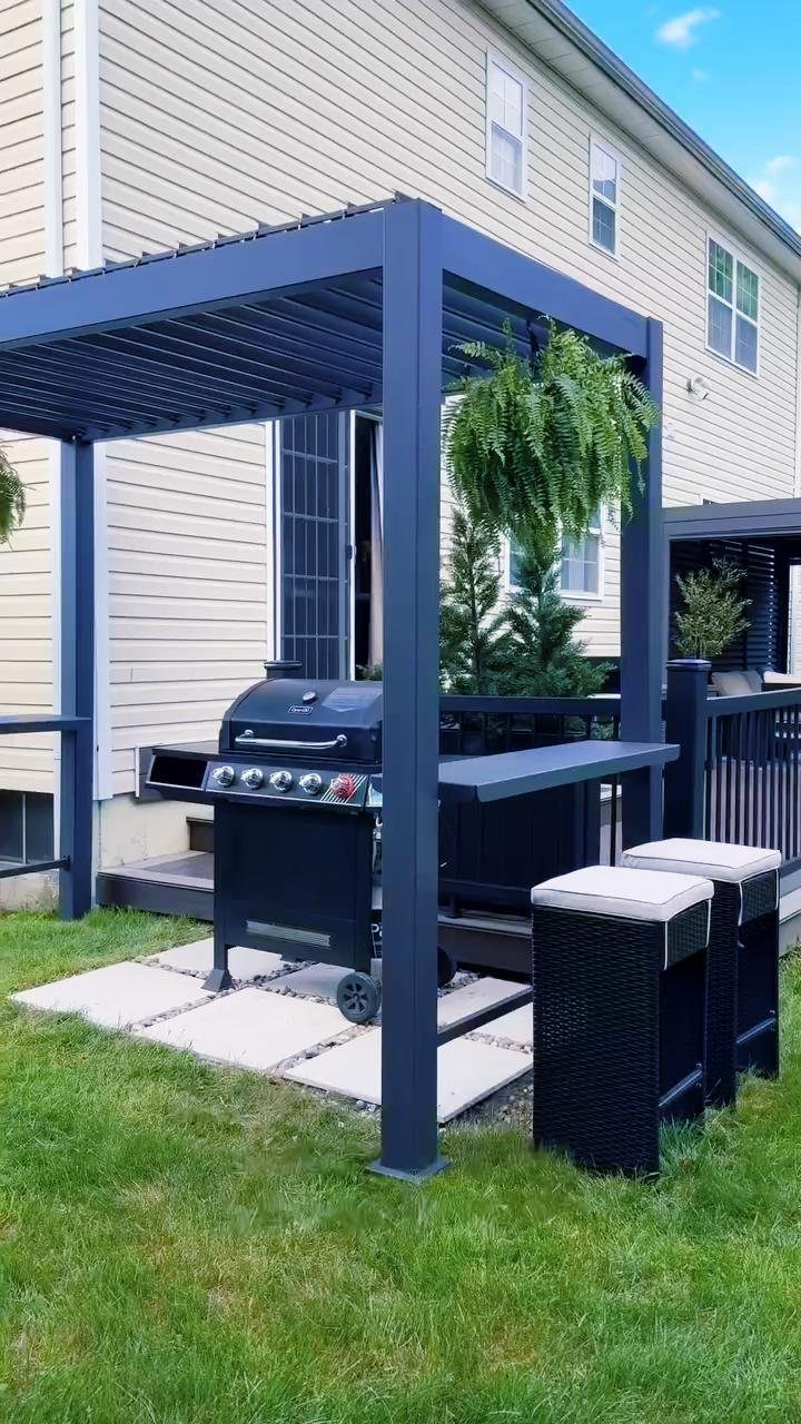 12 Backyard BBQ Ideas for Grill Area and Patio Layout 6 A dark blue metal pergola shading a black grill and seating area on a stone patio.