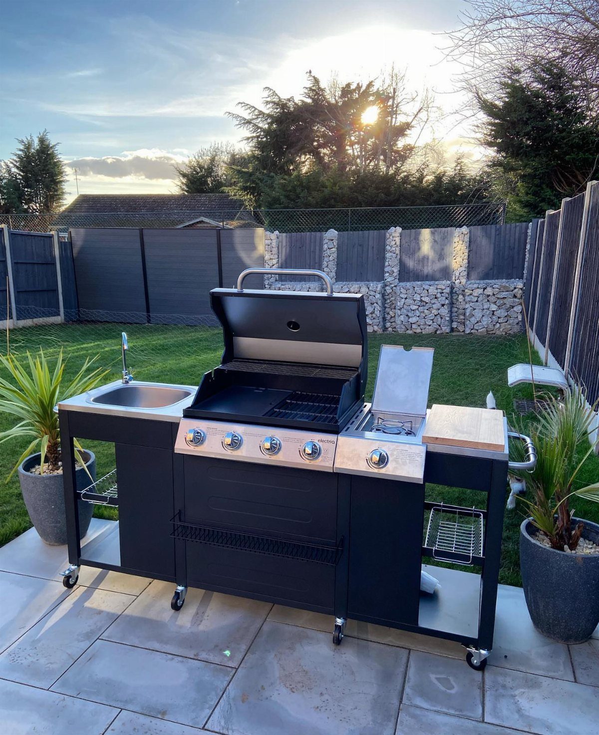 12 Backyard BBQ Ideas for Grill Area and Patio Layout 5 Black portable grill cart with a sink and burners on a stone patio outdoors.