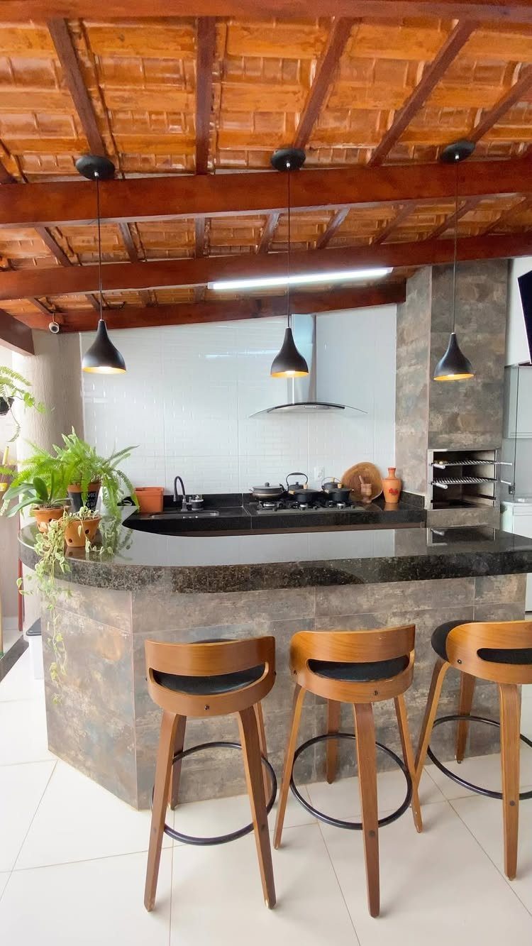 Outdoor kitchen with granite countertops, stone cabinetry, wooden bar stools, and a tiled wooden beam ceiling.