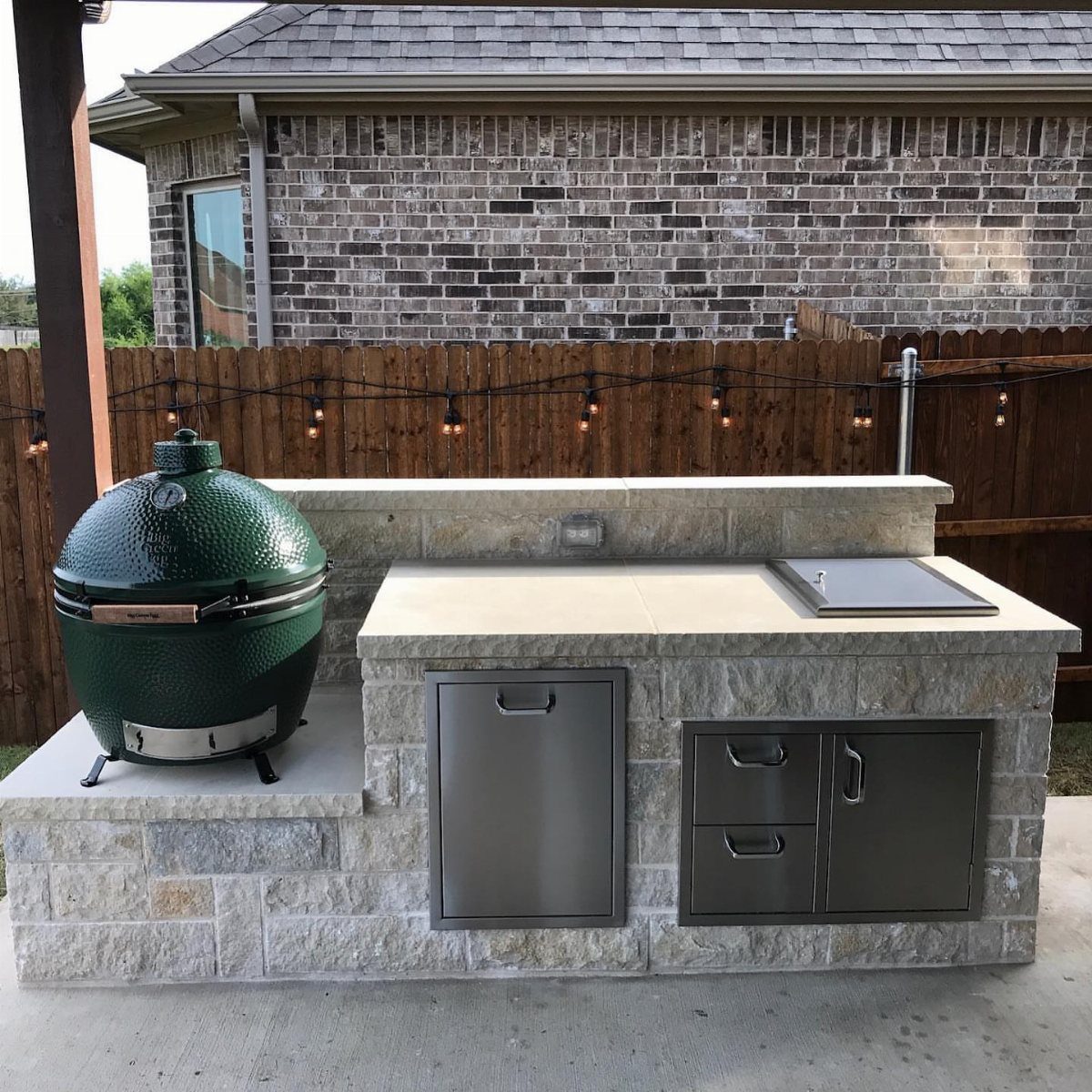 A stone outdoor kitchen island with a green ceramic grill and a black drop-in cooler.