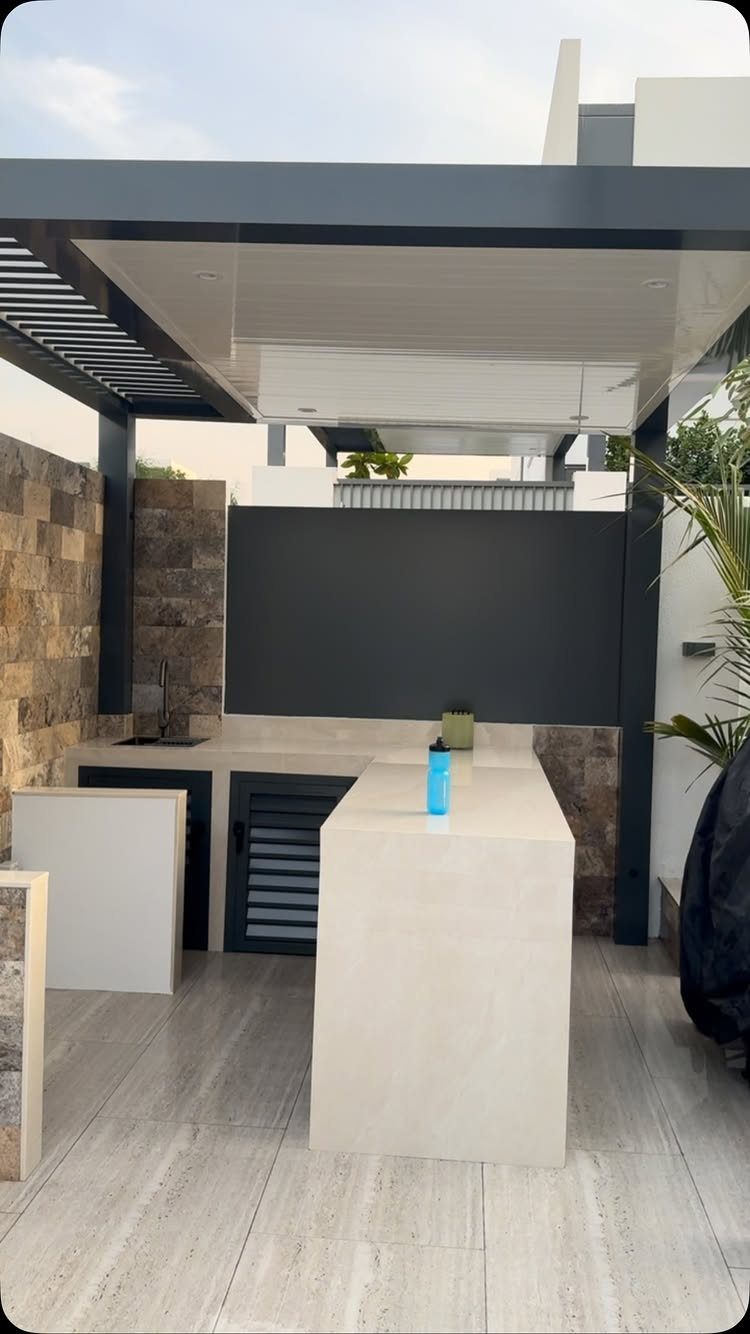 Modern outdoor kitchen with a large white stone island and dark metal pergola structure.