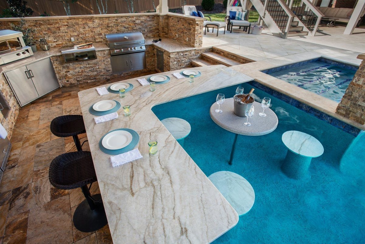 Backyard Pool Bar Ideas: 10 Upgrades for Summer Entertaining 7 A stone outdoor kitchen with a grill sits next to a curved swim-up pool bar.