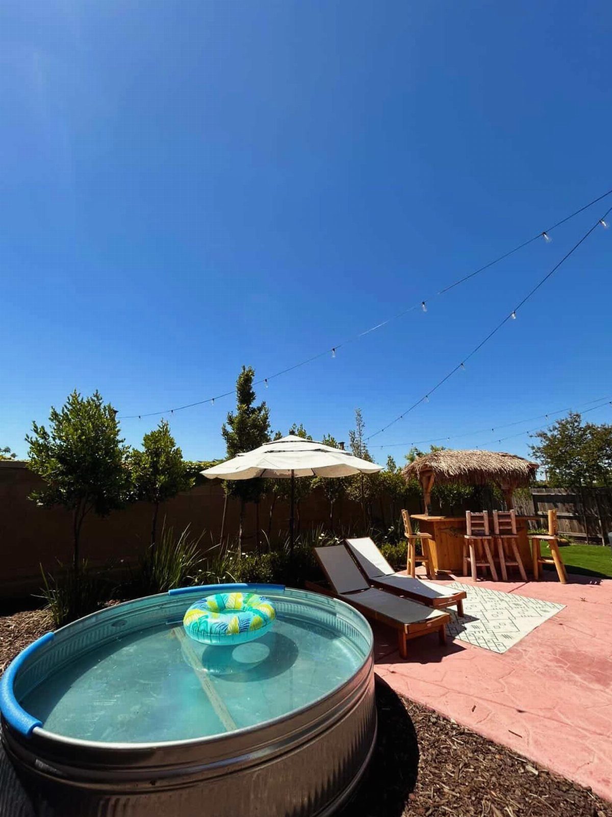 Backyard Pool Bar Ideas: 10 Upgrades for Summer Entertaining 2 A small round pool sits near lounge chairs and a thatched tiki-style bar.
