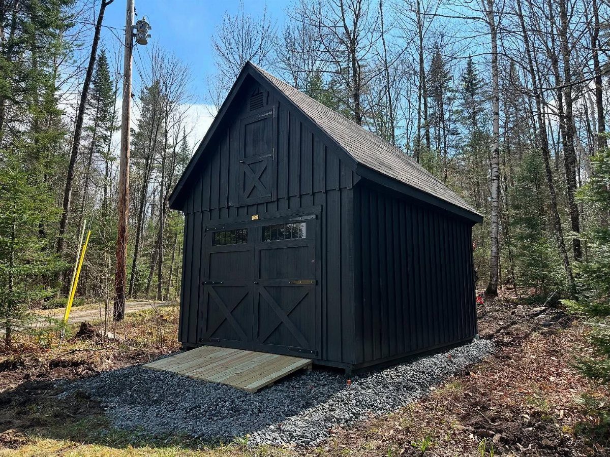 Board and Batten Shed: 5 Color Ideas That Work 2 A black board and batten wooden shed with double doors in a forest setting.