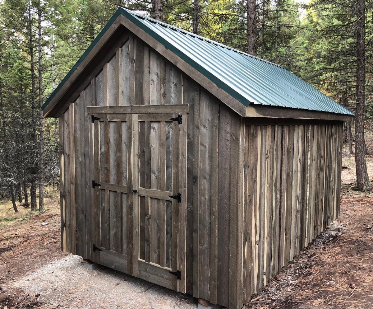 Board and Batten Shed: 5 Color Ideas That Work 5 A wooden storage shed with vertical planks and a green metal roof in a forest.