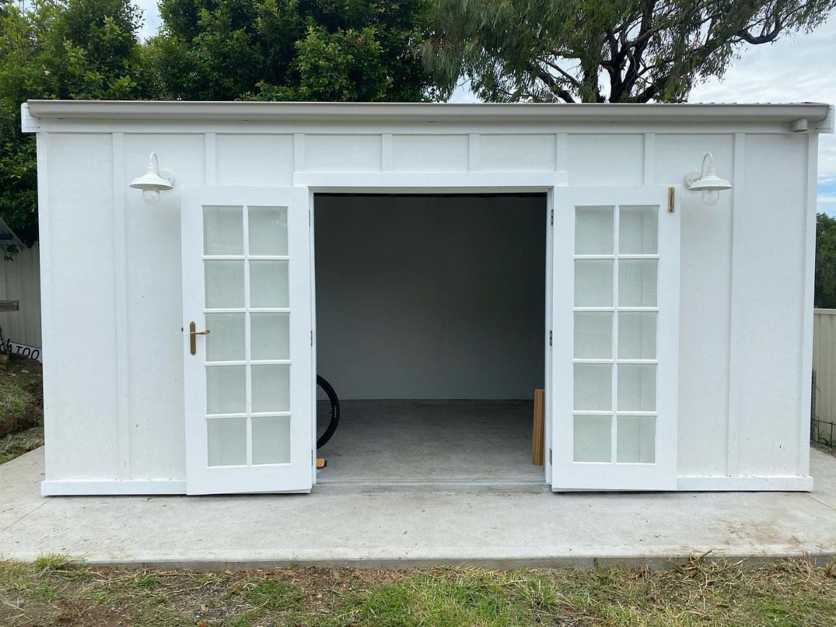 Board and Batten Shed: 5 Color Ideas That Work 1 White board and batten shed with open double doors revealing an empty interior space.