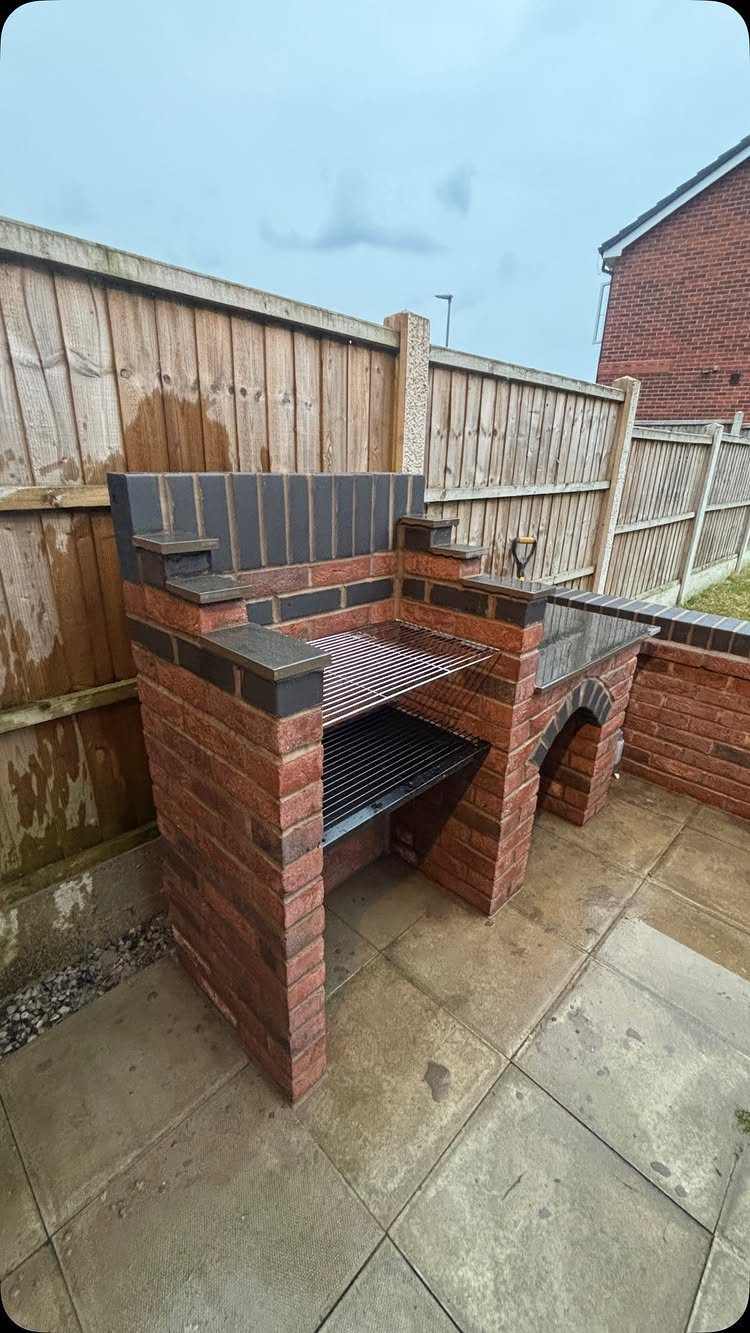 10 Brick BBQ Ideas: From Classic Pits to Pizza-Oven Combos 9 A red brick outdoor barbecue with dark grey tiled surfaces and a metal grill grate.