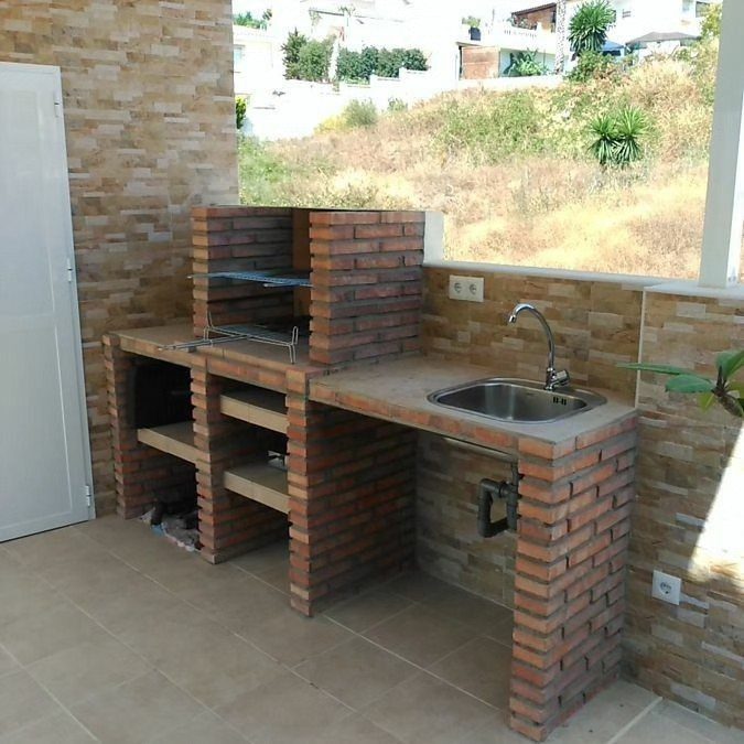 10 Brick BBQ Ideas: From Classic Pits to Pizza-Oven Combos 6 A brick outdoor kitchen unit with a grill, shelves, and a built-in sink on a patio.