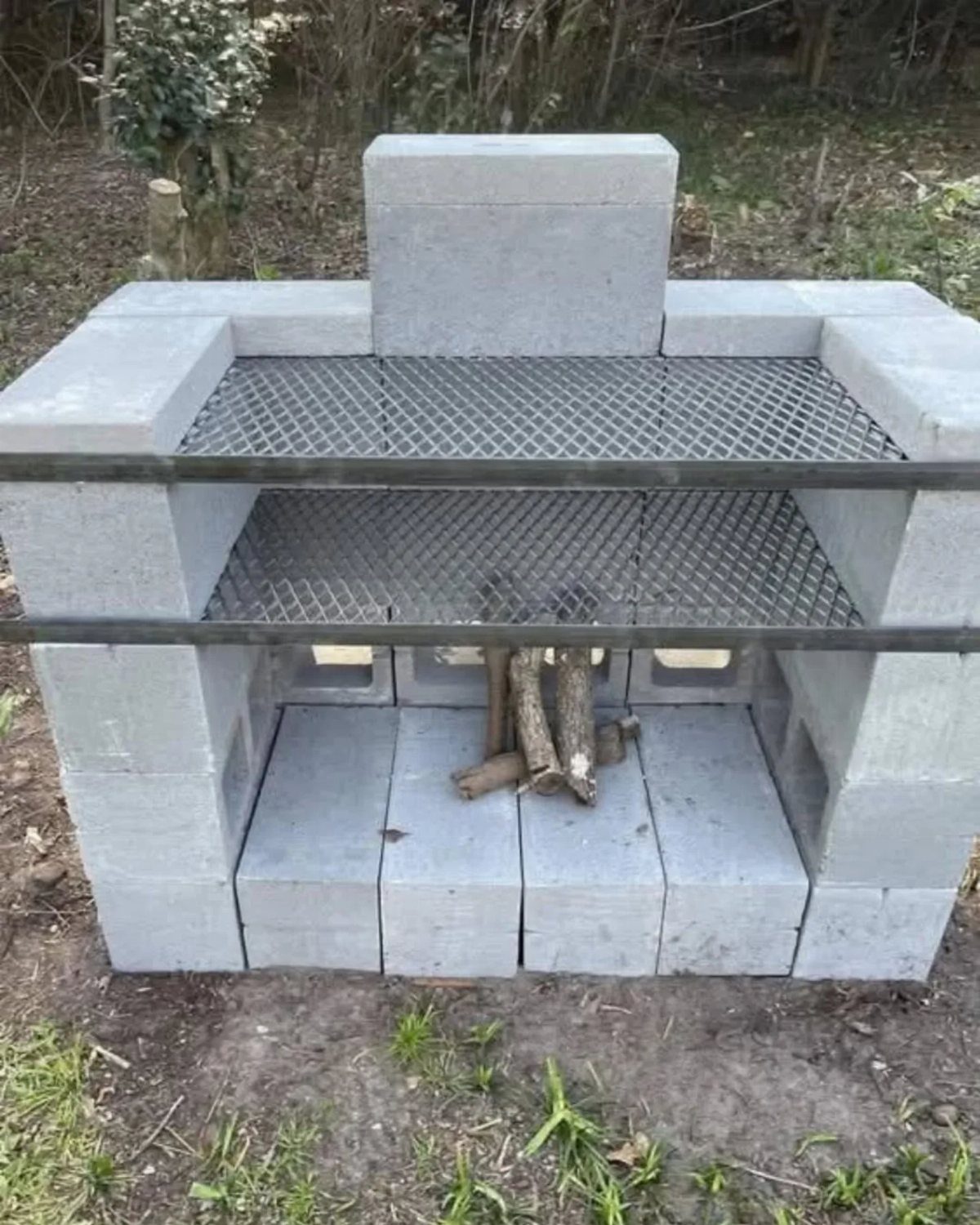 10 Brick BBQ Ideas: From Classic Pits to Pizza-Oven Combos 5 A DIY barbecue grill built from grey cinder blocks with two metal mesh grates and firewood underneath.