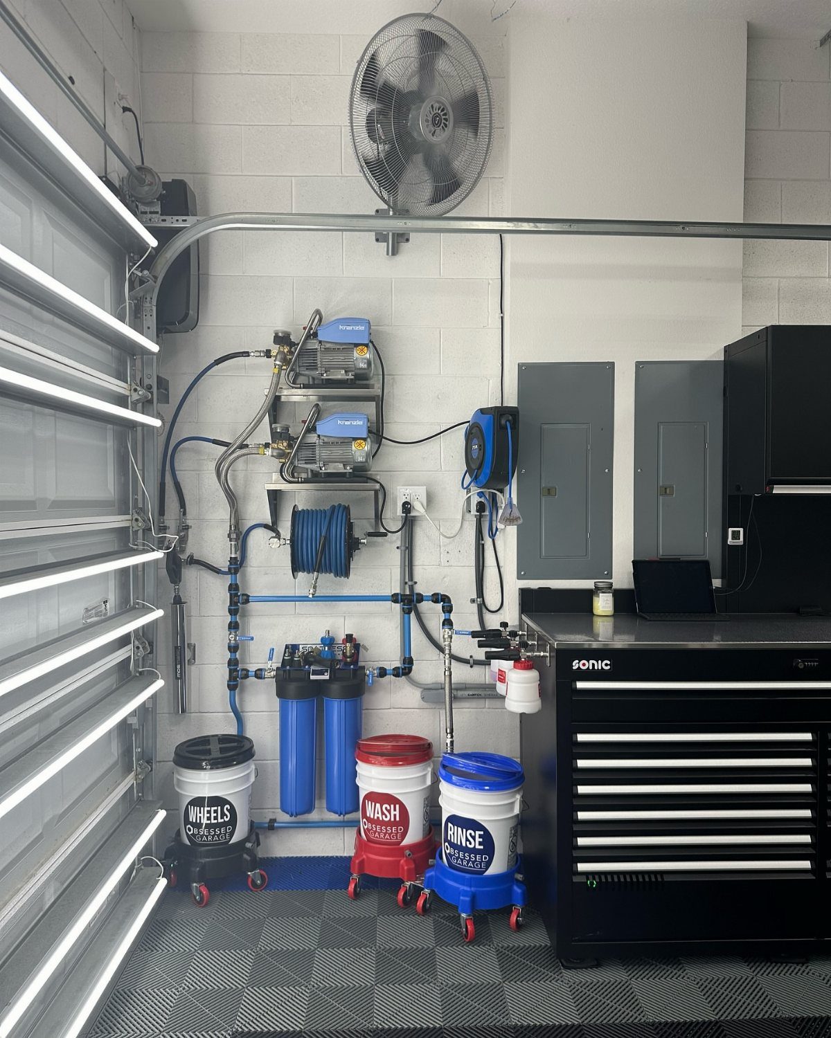 Organized garage utility station with water filtration, rolling buckets, and a large black tool chest.