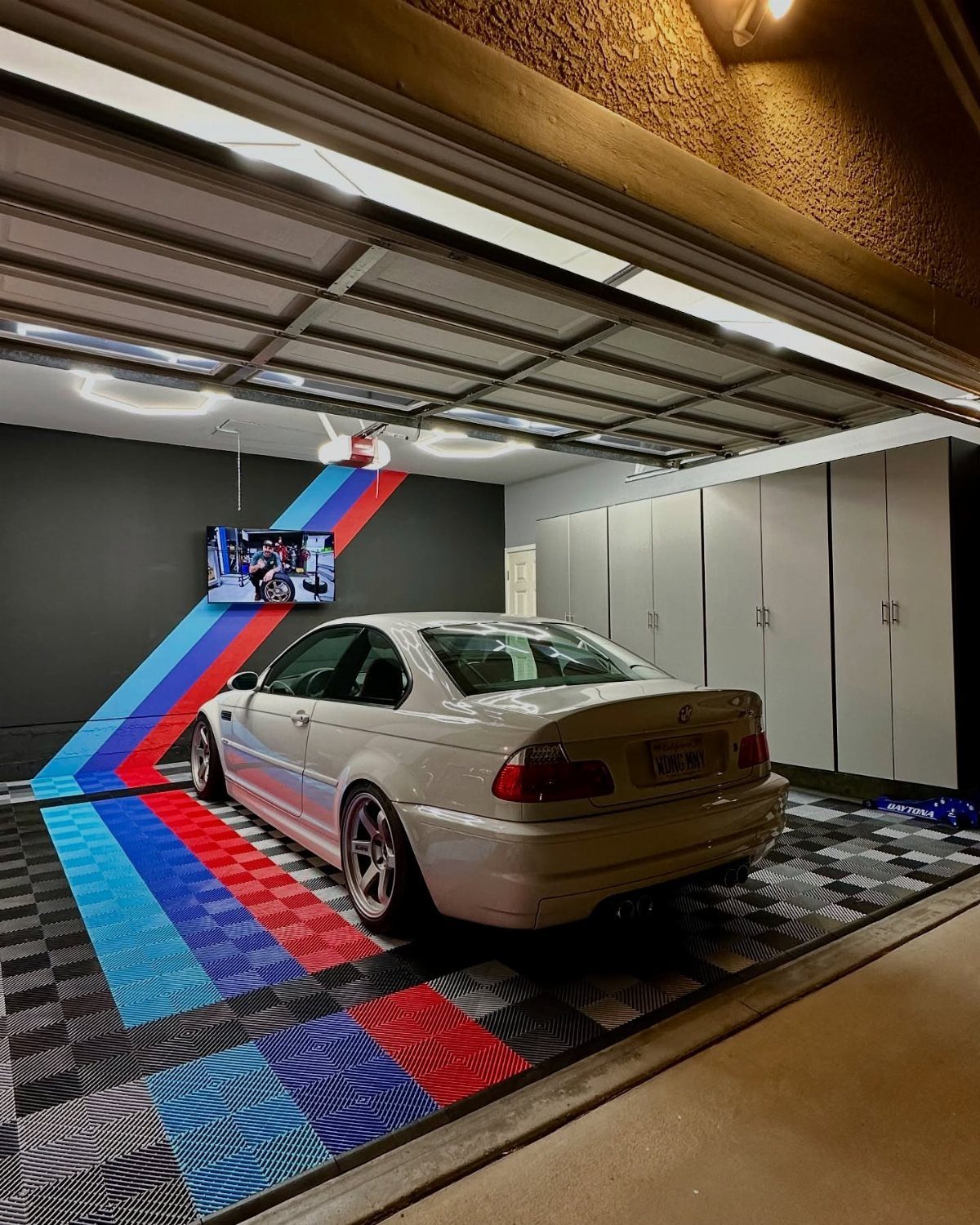 A white BMW parked in a modern garage with colorful striped floor tiles and white storage cabinets.