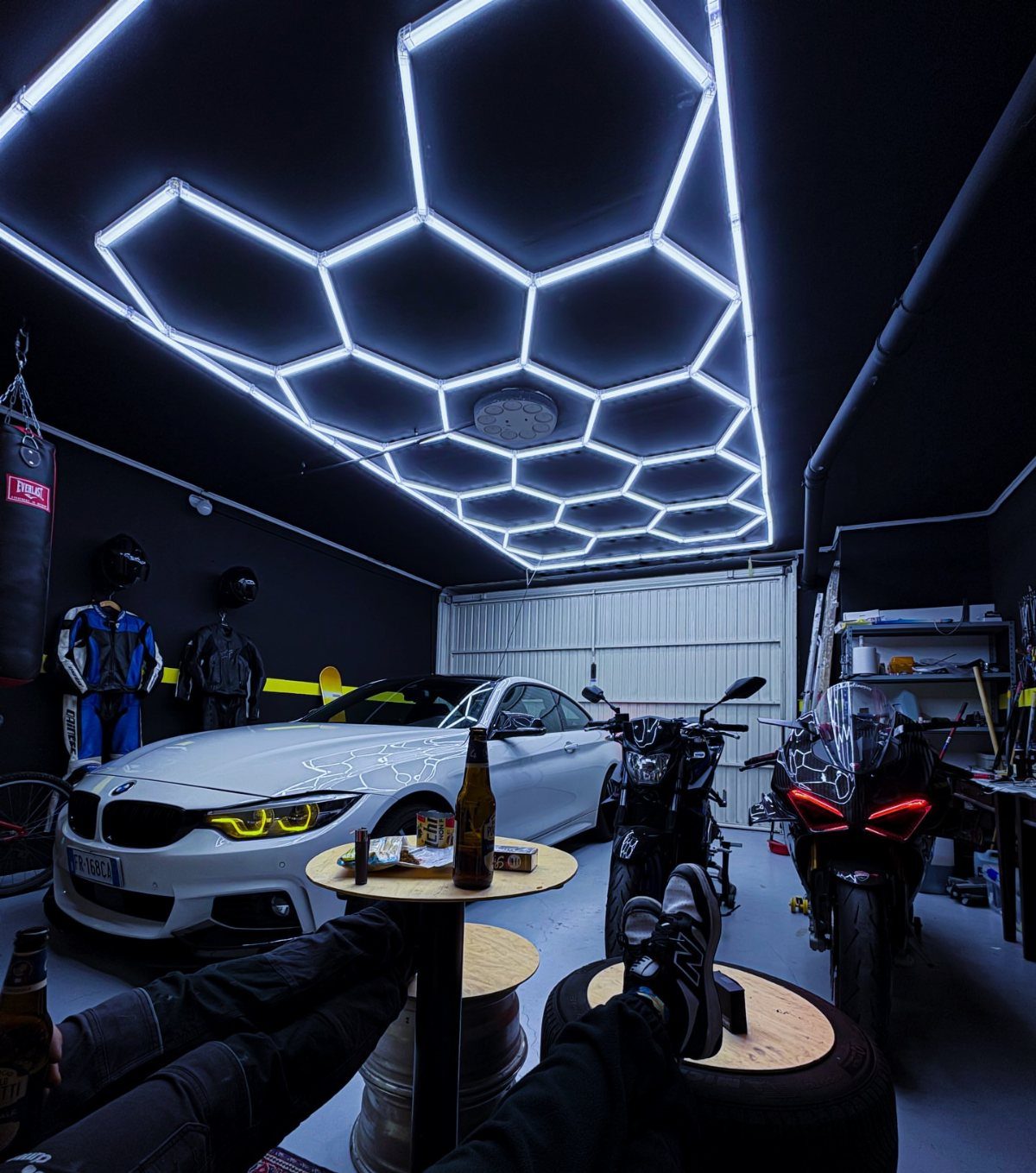 White BMW and motorcycles in a garage with hexagonal LED ceiling lights.
