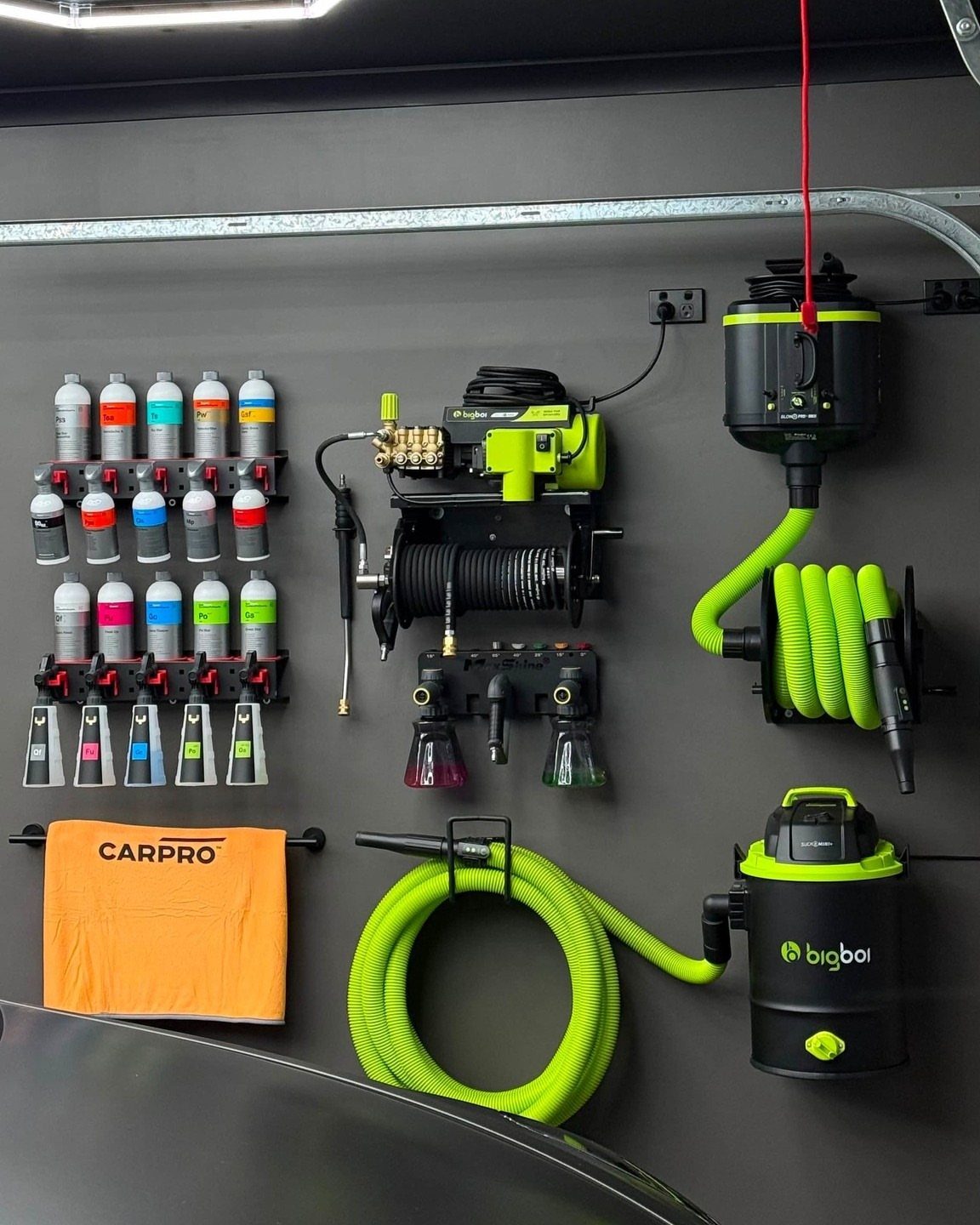 Organized cleaning supplies and equipment mounted on a dark grey garage wall.