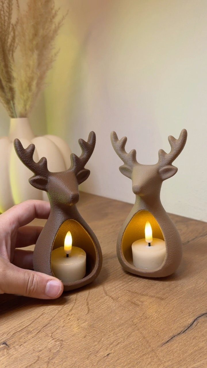 Two ceramic reindeer candle holders with lit tea lights on a wooden table.