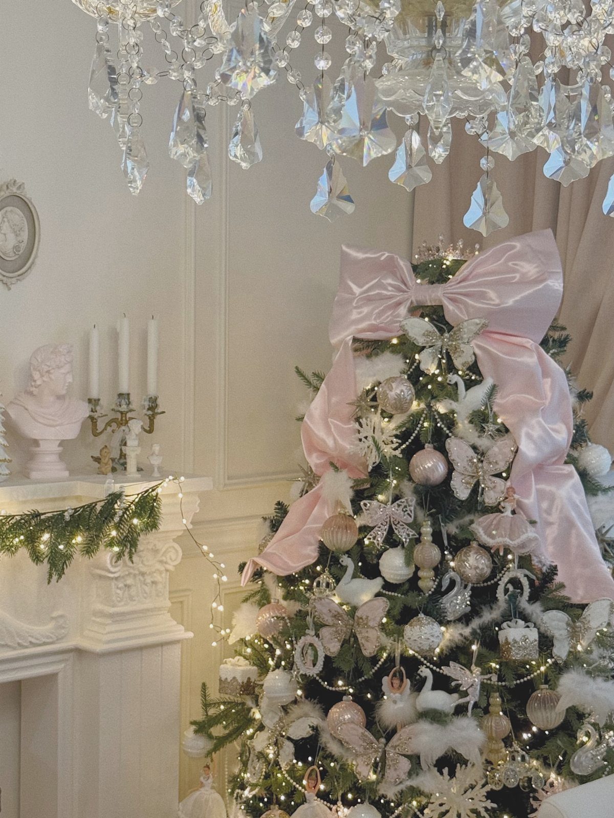 A decorated Christmas tree with pink bows, white swan ornaments, and a crystal chandelier hanging above.