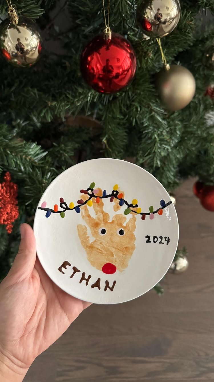12 Christmas Family Craft Ideas: Projects for All Ages 7 A hand holding a white plate decorated with a reindeer handprint craft.
