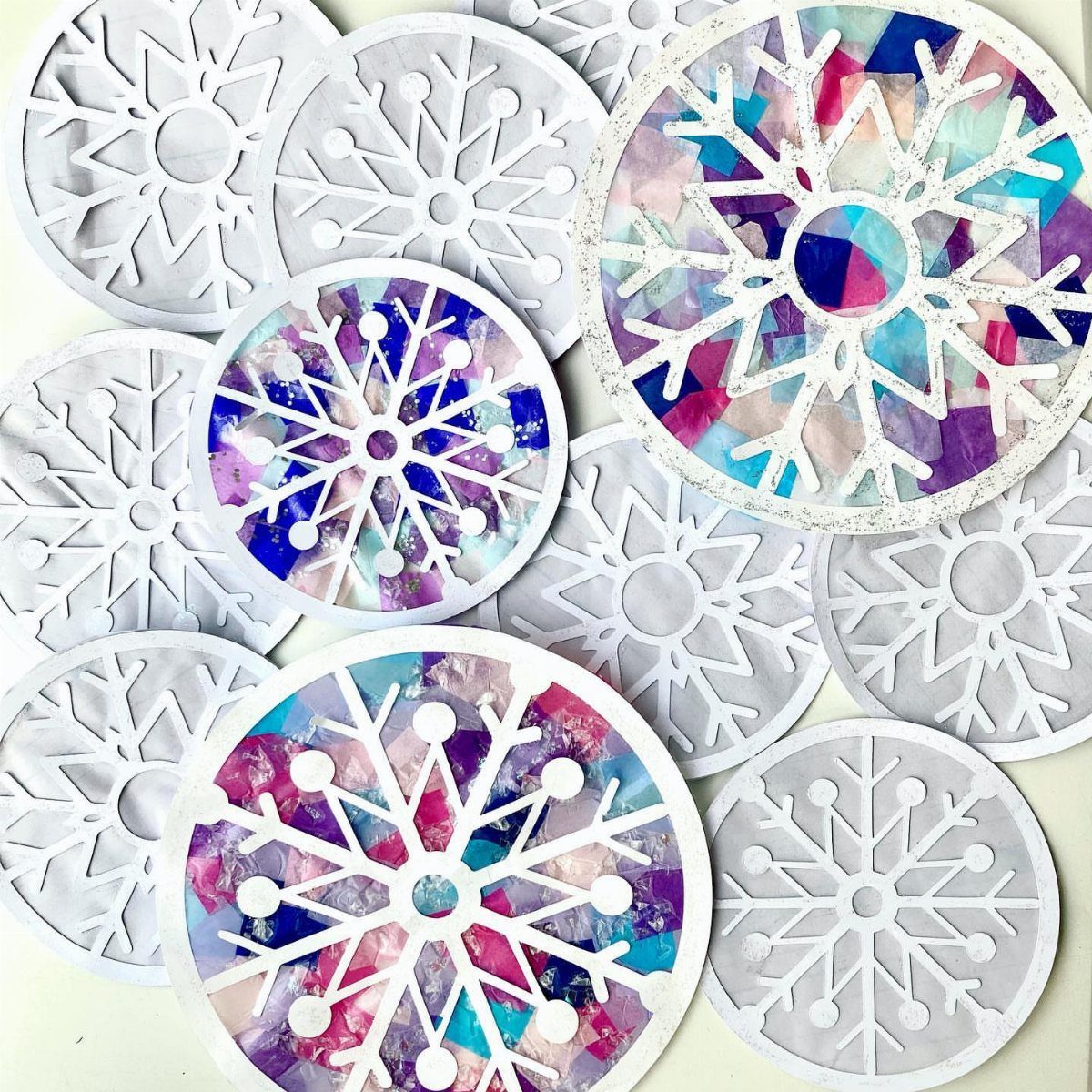 12 Christmas Family Craft Ideas: Projects for All Ages 2 Various white and colorful stained-glass style paper snowflake crafts scattered on a light background.