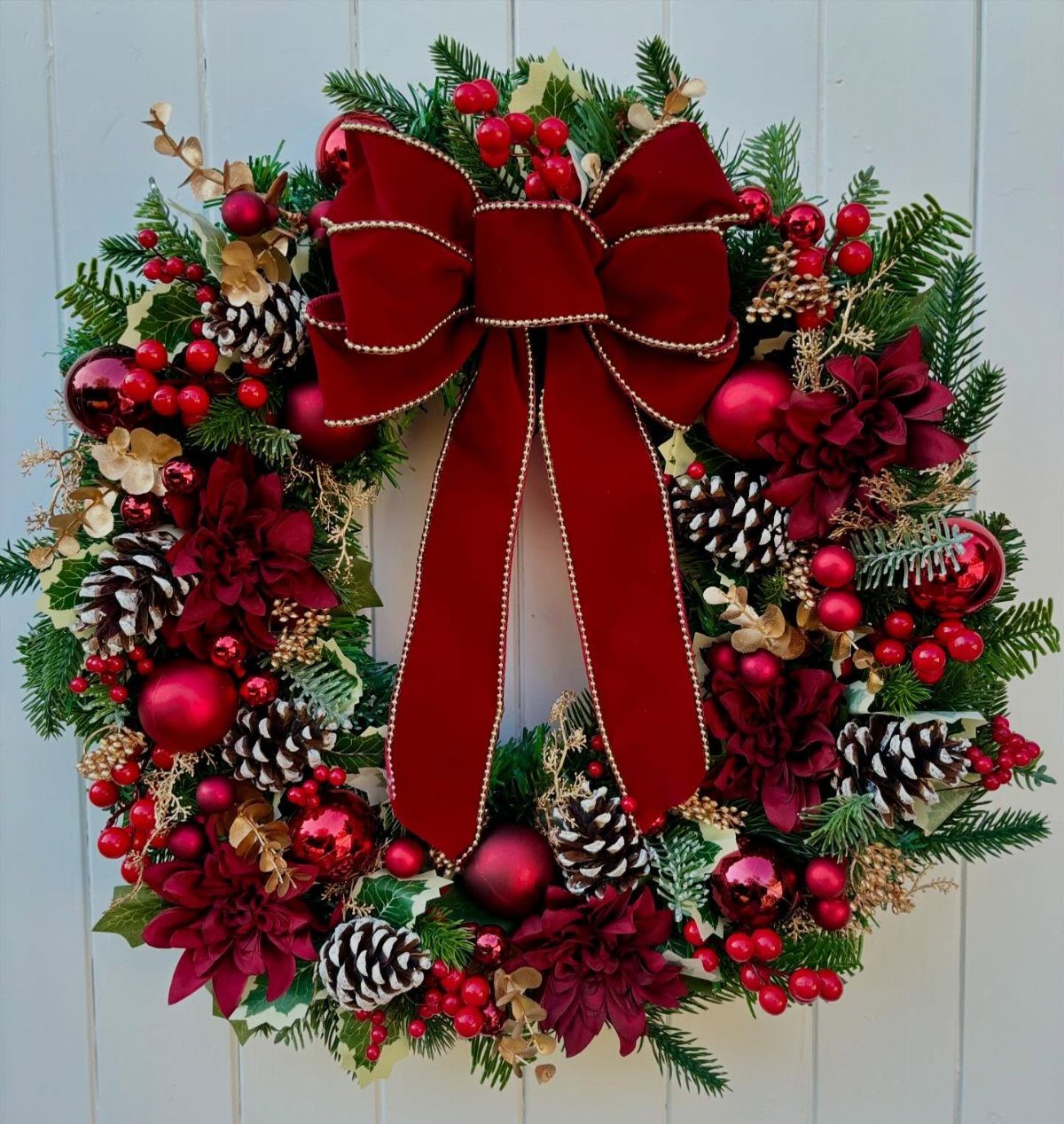 12 Christmas Family Craft Ideas: Projects for All Ages 5 A festive Christmas wreath decorated with red berries, pinecones, ornaments, and a large red velvet bow.