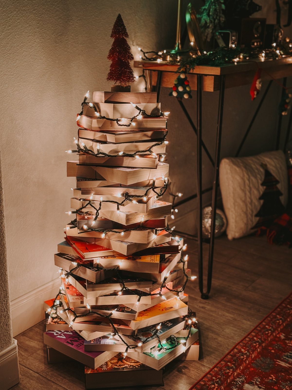 A Christmas tree constructed from stacked books decorated with glowing white string lights.
