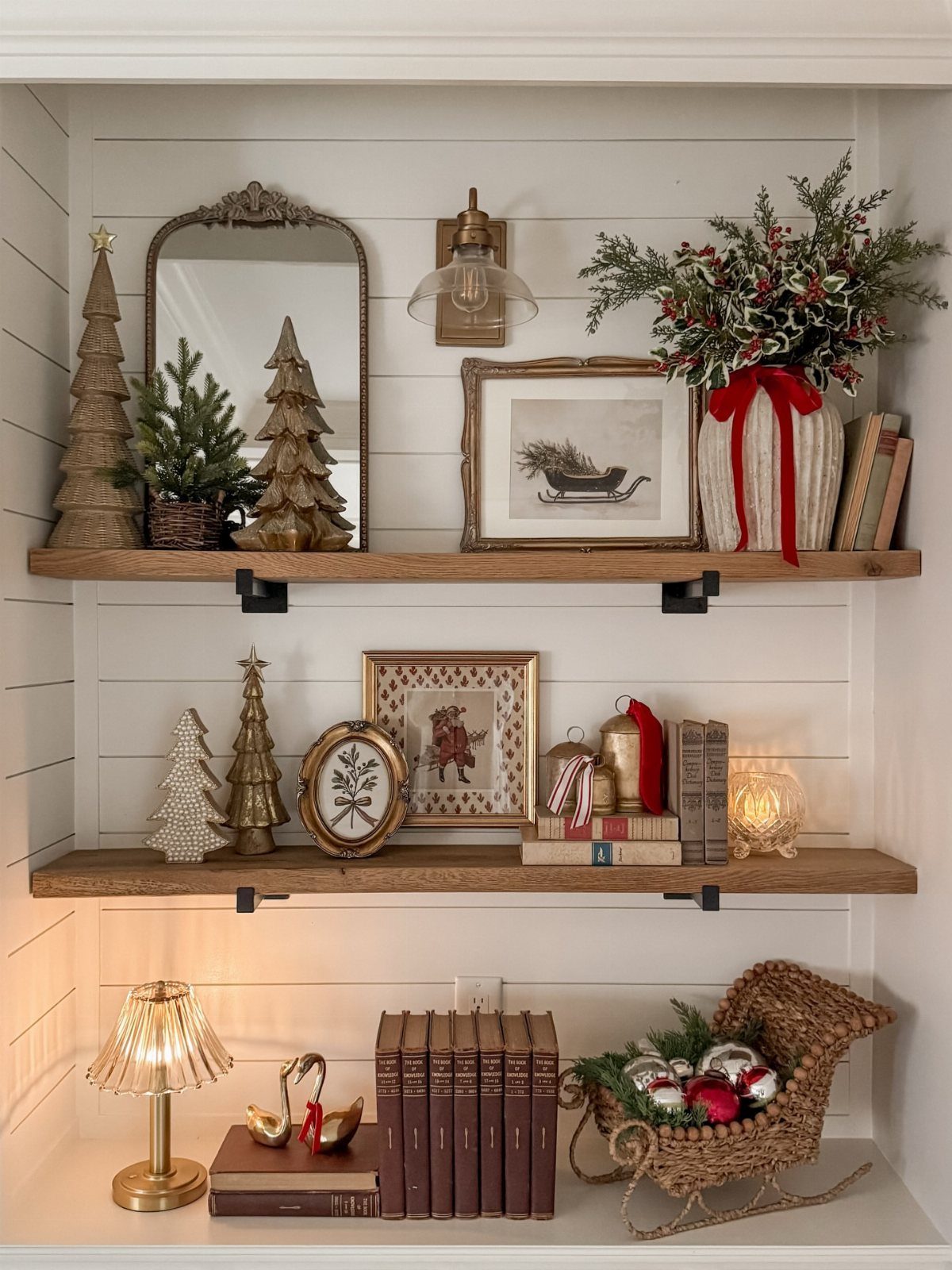 Various vintage Christmas decorations arranged on three wooden shelves against a white shiplap wall.