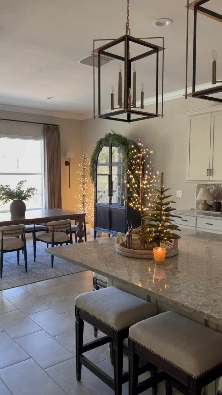 Tall twig sculptures wrapped in warm string lights stand in a decorated dining area.
