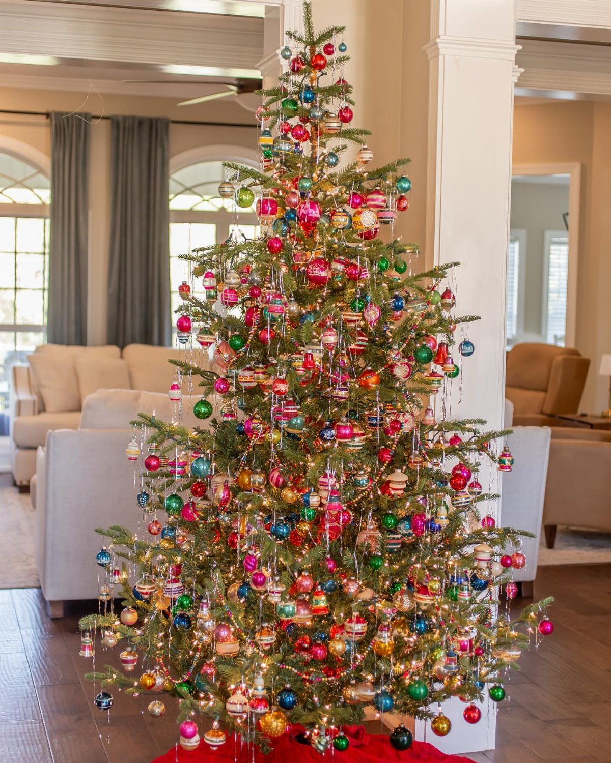 A decorated Christmas tree featuring many colorful vintage glass ornaments and warm glowing string lights.