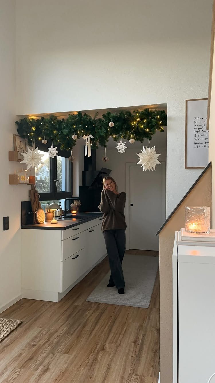 Green evergreen garland with fairy lights and white star ornaments hanging above a kitchen counter.