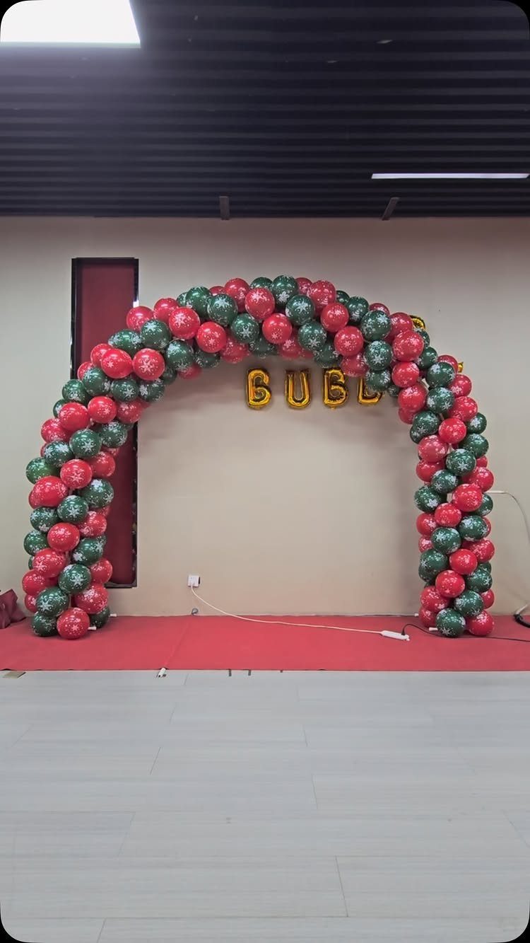 A large archway made of red and green glittery balloons against a neutral wall.