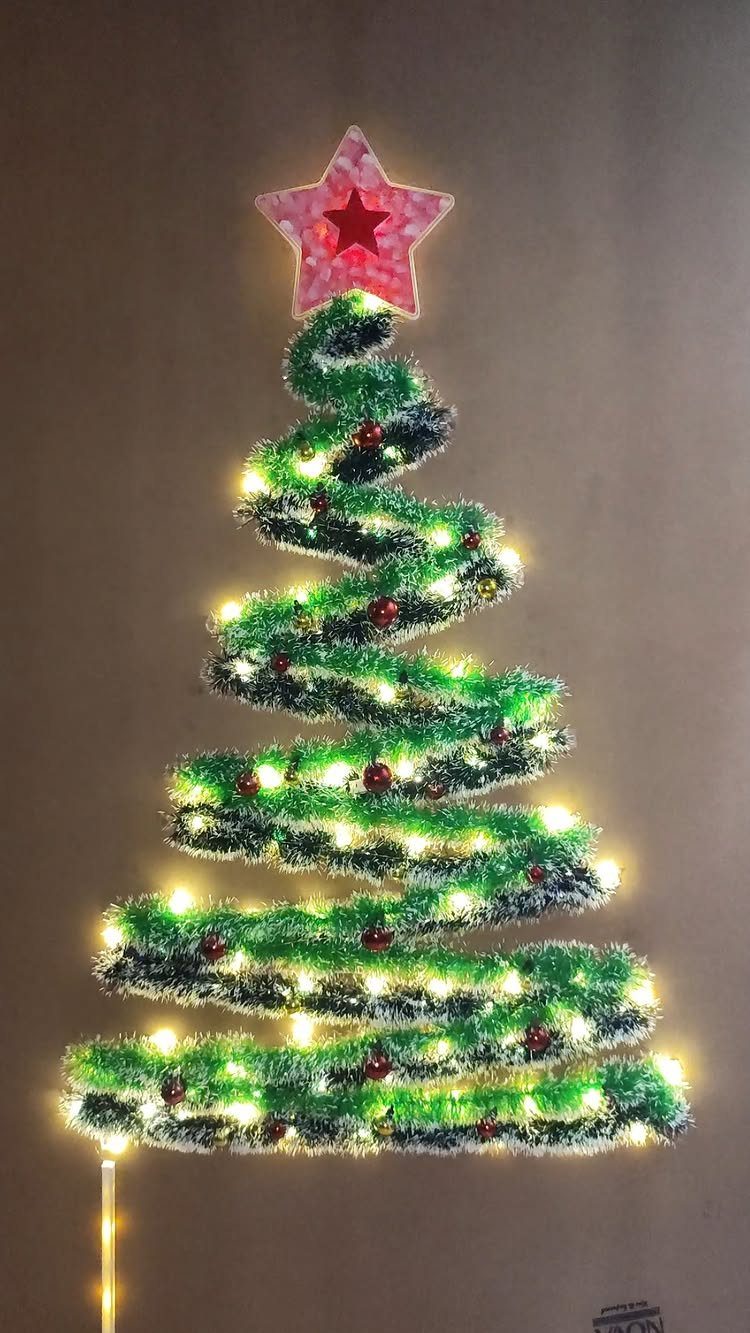 A spiral-shaped Christmas tree made of green tinsel and lights on a wall.