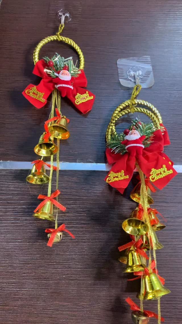 Two gold and red Christmas ornaments with hanging jingle bells against a dark wood background.