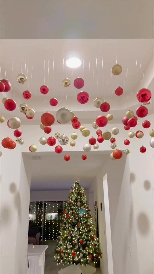 Red and gold Christmas ornaments hanging from a ceiling above a decorated Christmas tree.