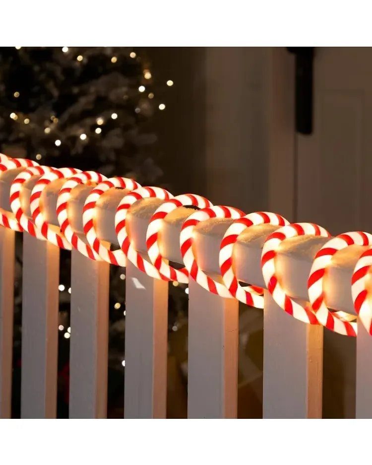 Glowing red and white striped candy cane decorations lined up along a white wooden railing at night.