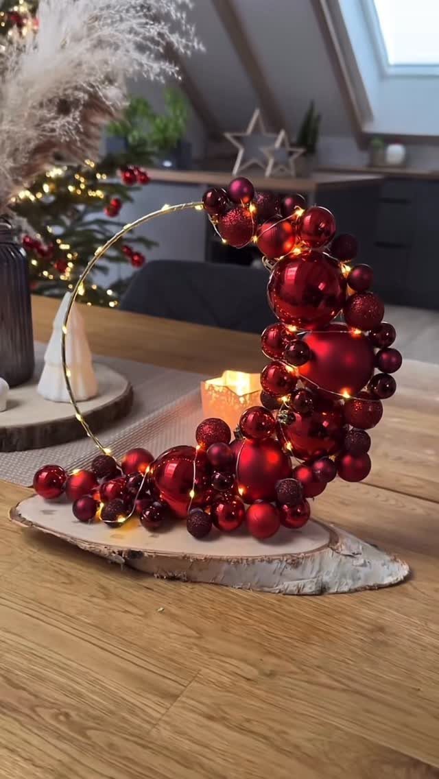Red Christmas ornament crescent decoration with warm lights on a wooden table surface.