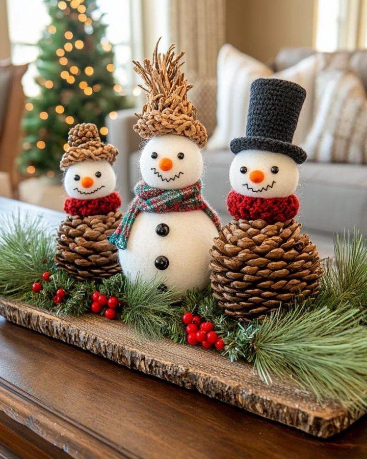 Three pinecone snowmen with felt bodies and festive hats resting on an evergreen decorated wooden tray.