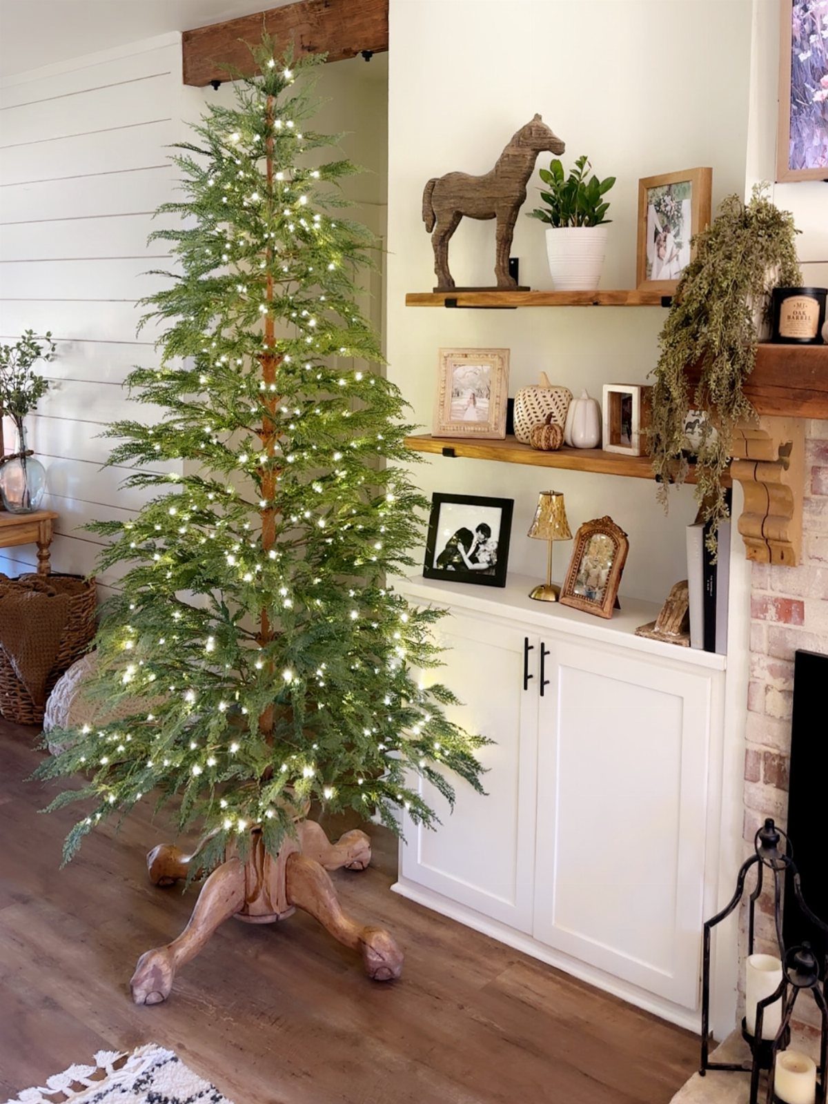 A lit Christmas tree sits on a large, decorative antique wooden tree stand indoors.