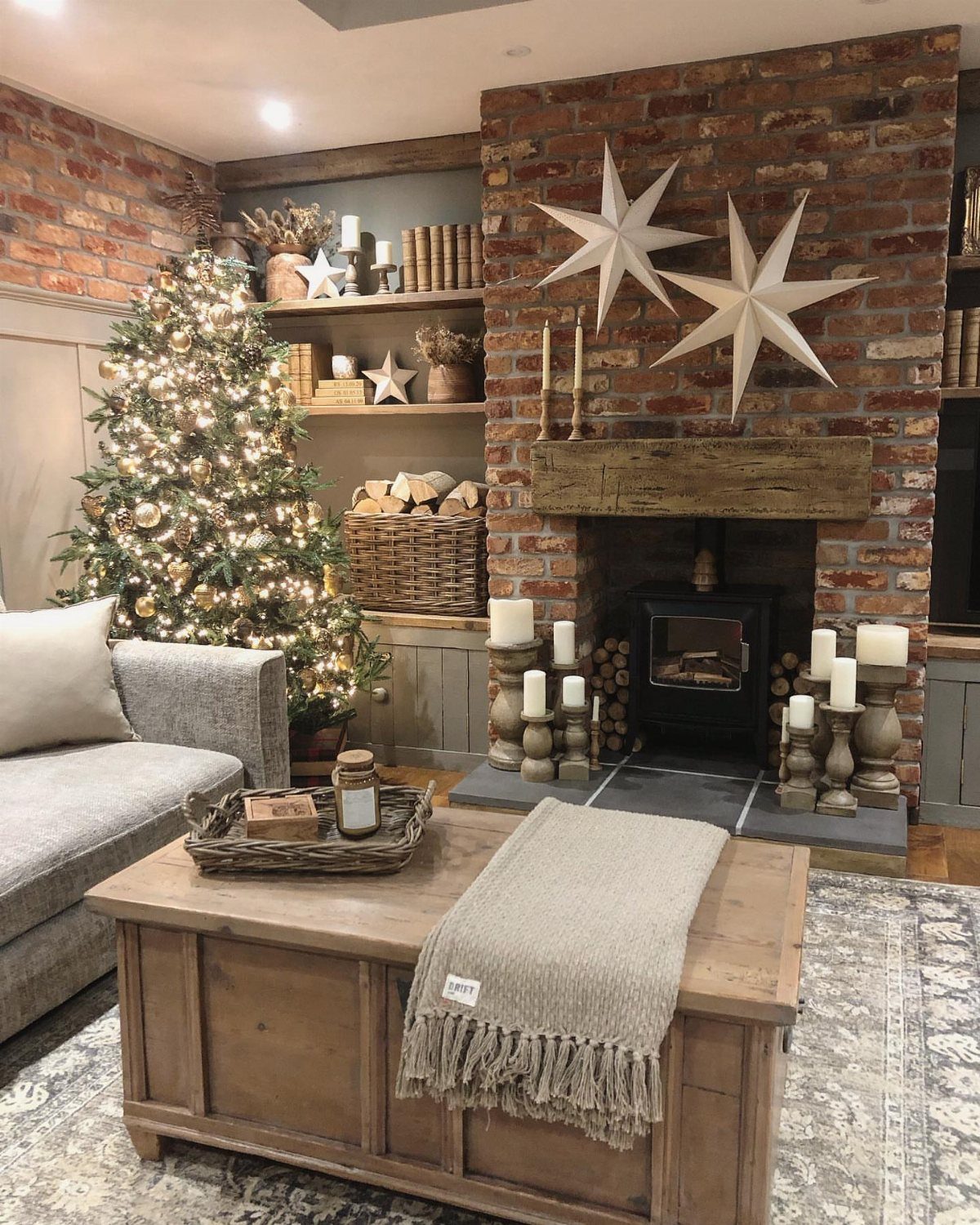 A decorated Christmas tree stands next to a brick fireplace with large white star ornaments.