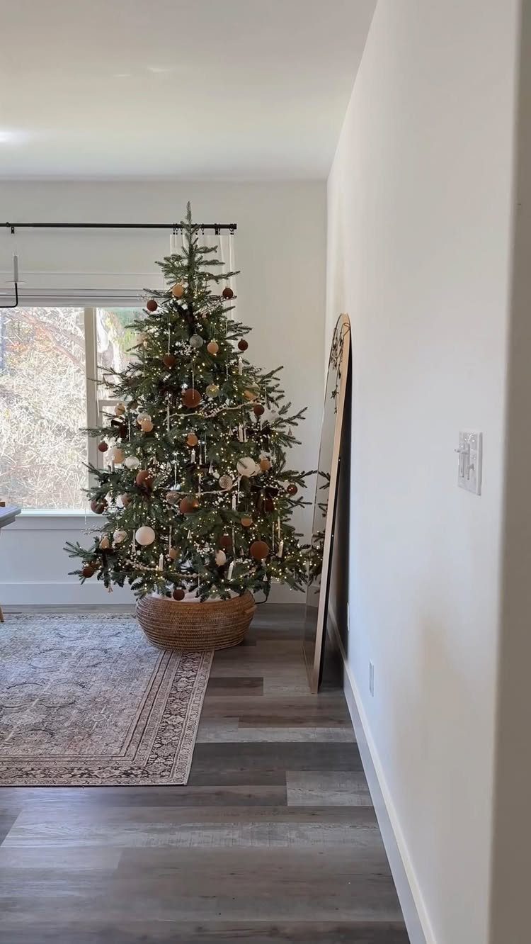 A decorated Christmas tree sitting in a large woven wicker basket on a rug.